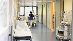 Im Krankenhausflur: Zwei Pflegekräfte schieben ein Patientenbett.