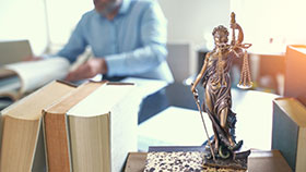 Foto: Schreibtisch mit mehreren Büchern und Figur einer Justitia